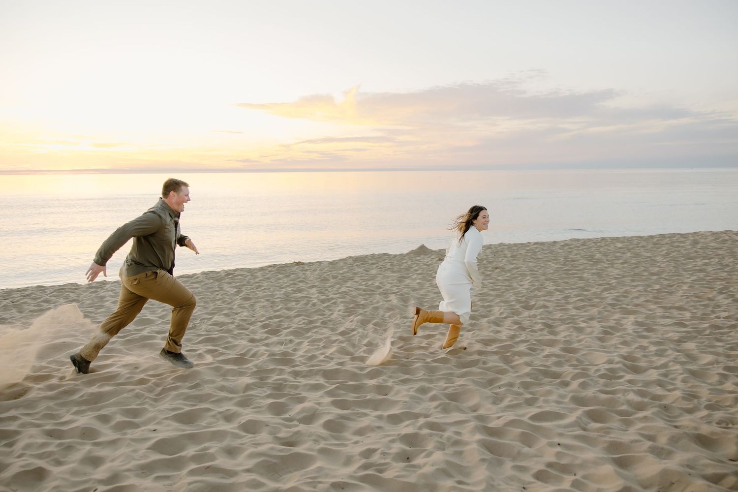 Couple running playfully on a sandy beach during golden hour sunset.
