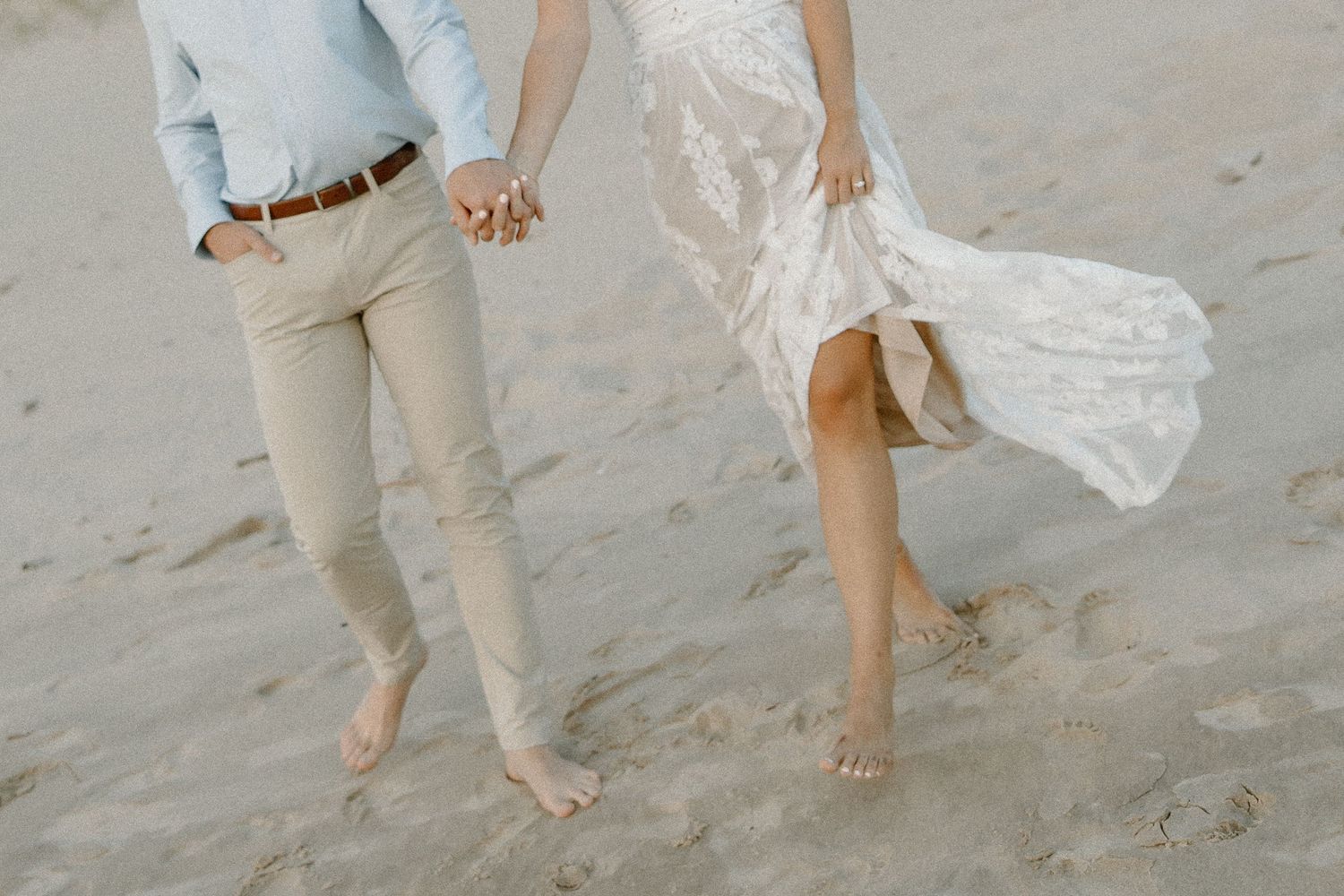 Close-up of bare feet walking on beach sand with flowing white dress.