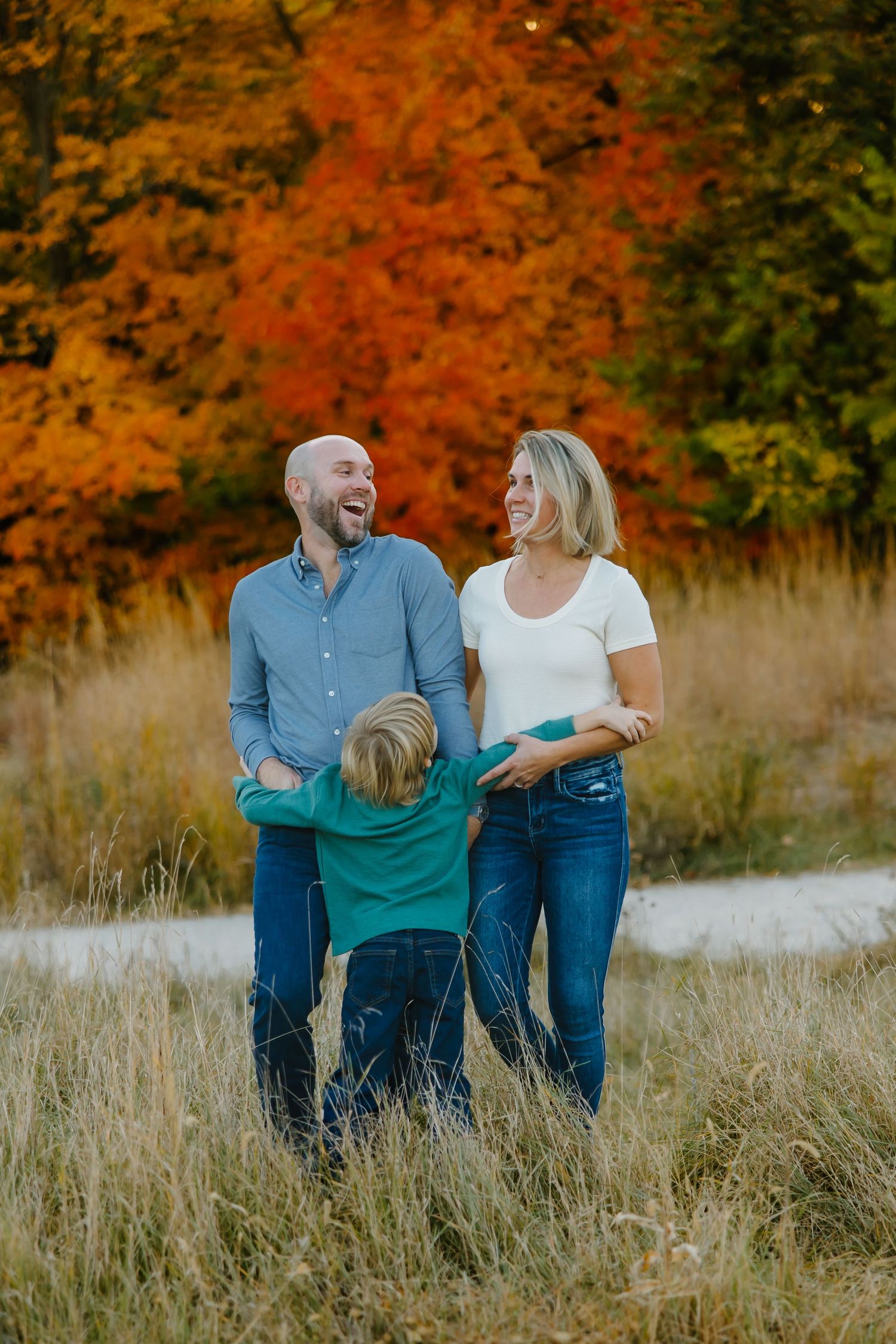 Family enjoying autumn scenery together in a grassy field with vibrant orange fall foliage in the background.