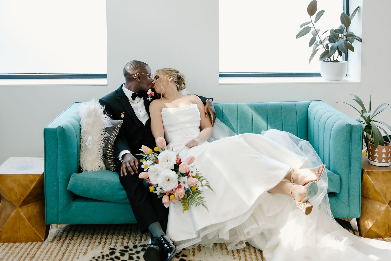 Wedding couple sharing intimate moment on turquoise couch in bright modern setting.
