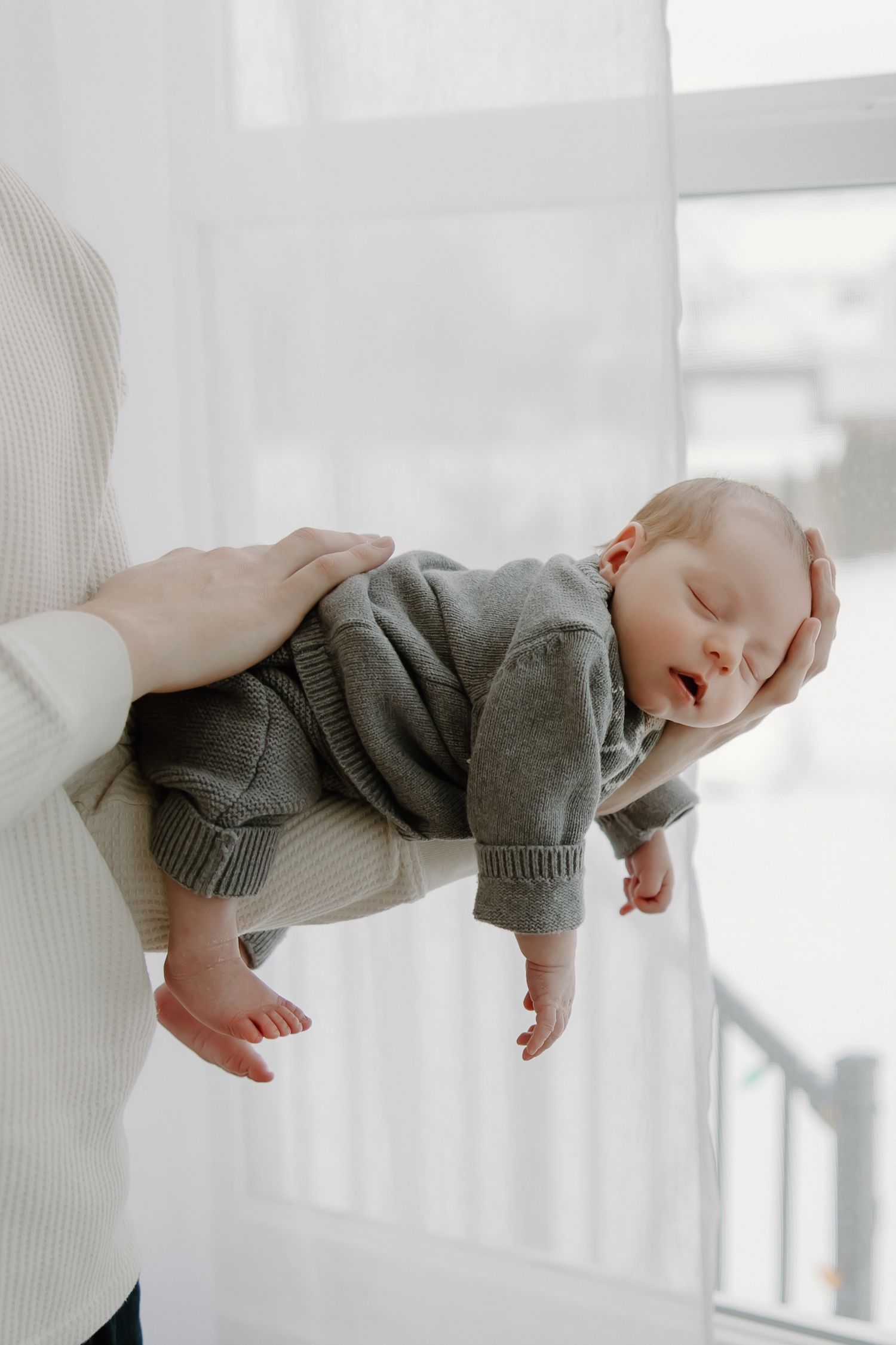 A newborn baby wearing a gray sweater being cradled against white fabric in multiple angles.