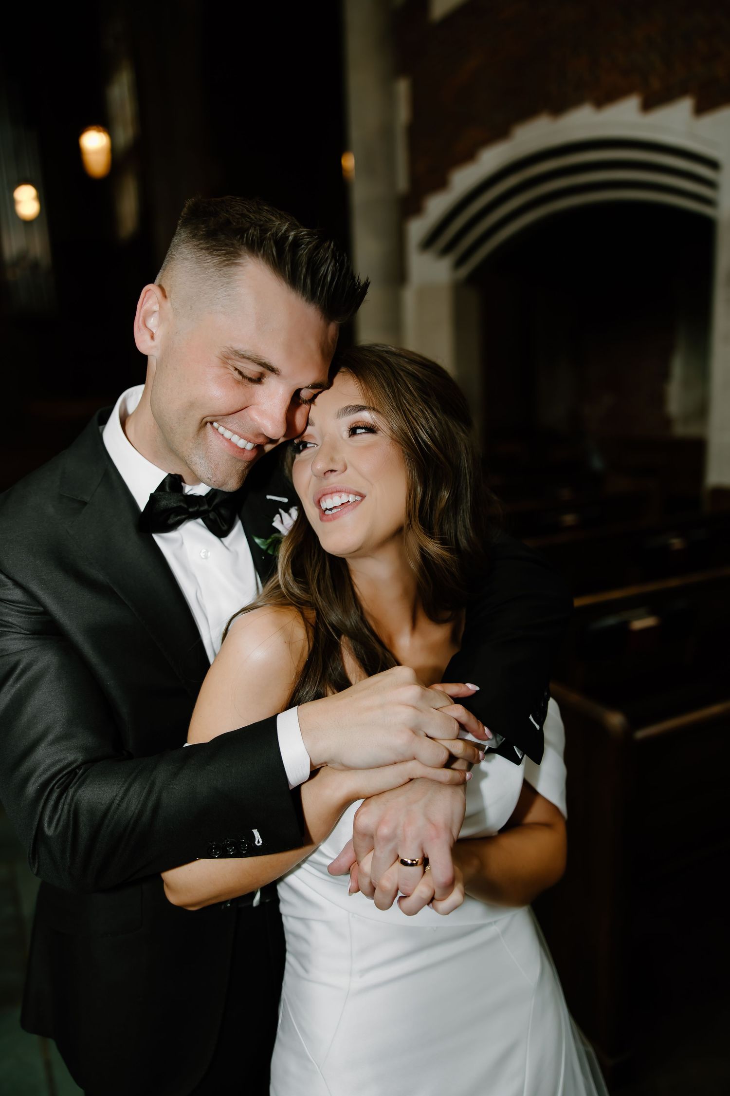 Intimate wedding couple moment captured in dramatic lighting inside historic building.
