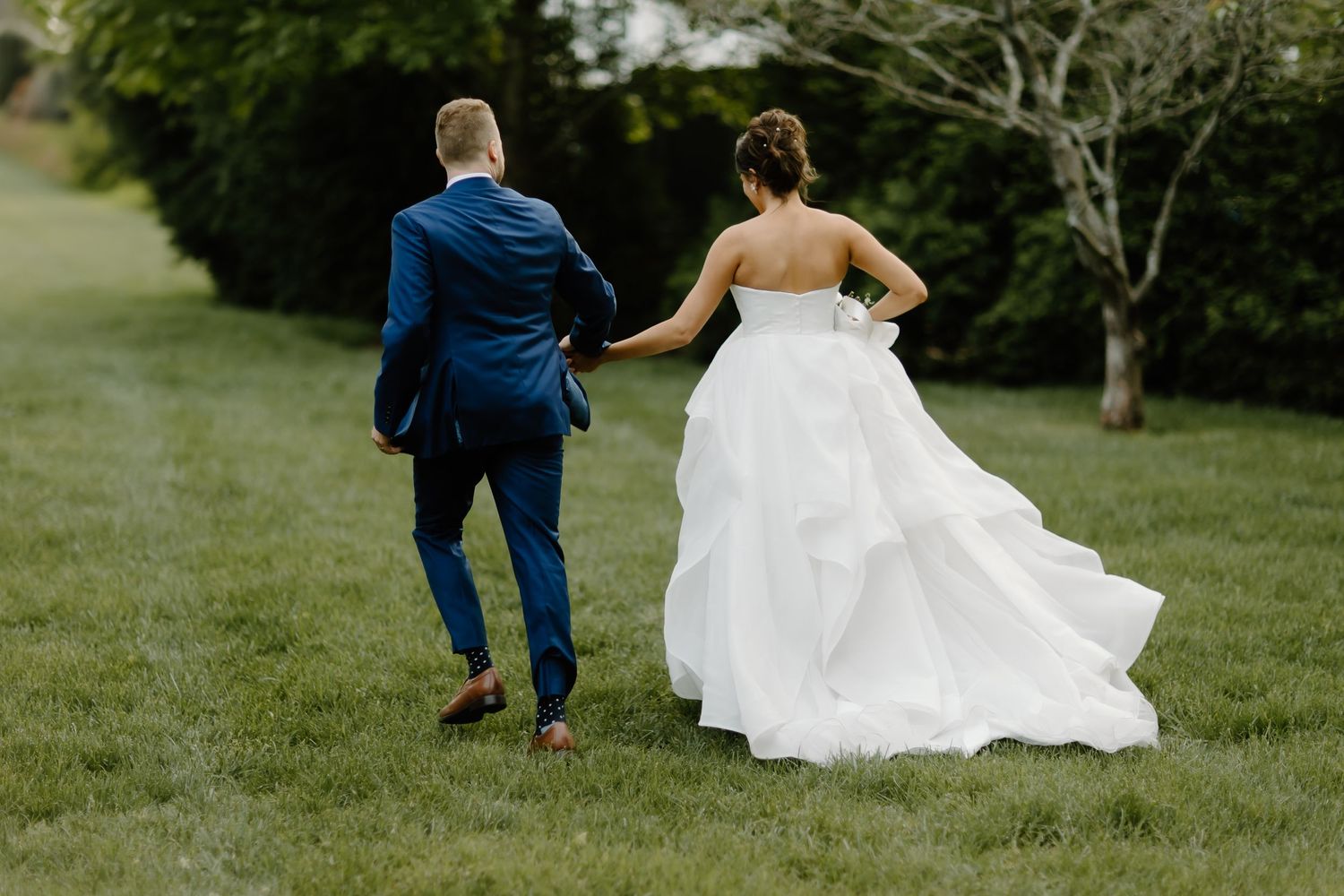 Couple walking across grassy lawn with flowing white wedding dress.