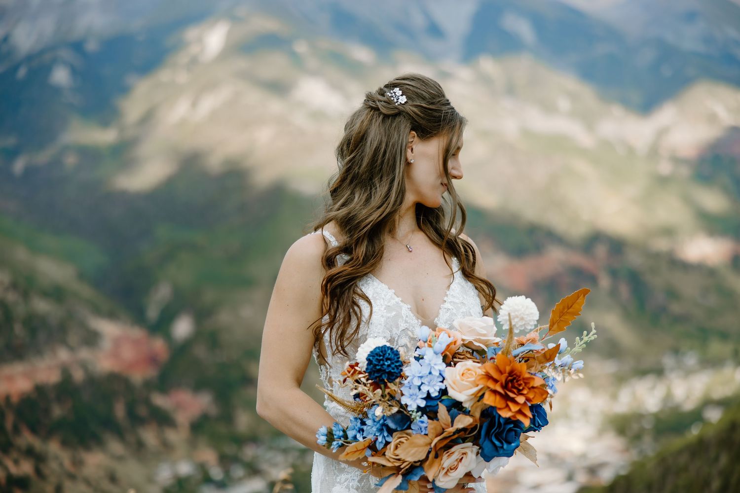 A bride holds a vibrant blue and orange bouquet against a mountainous backdrop.