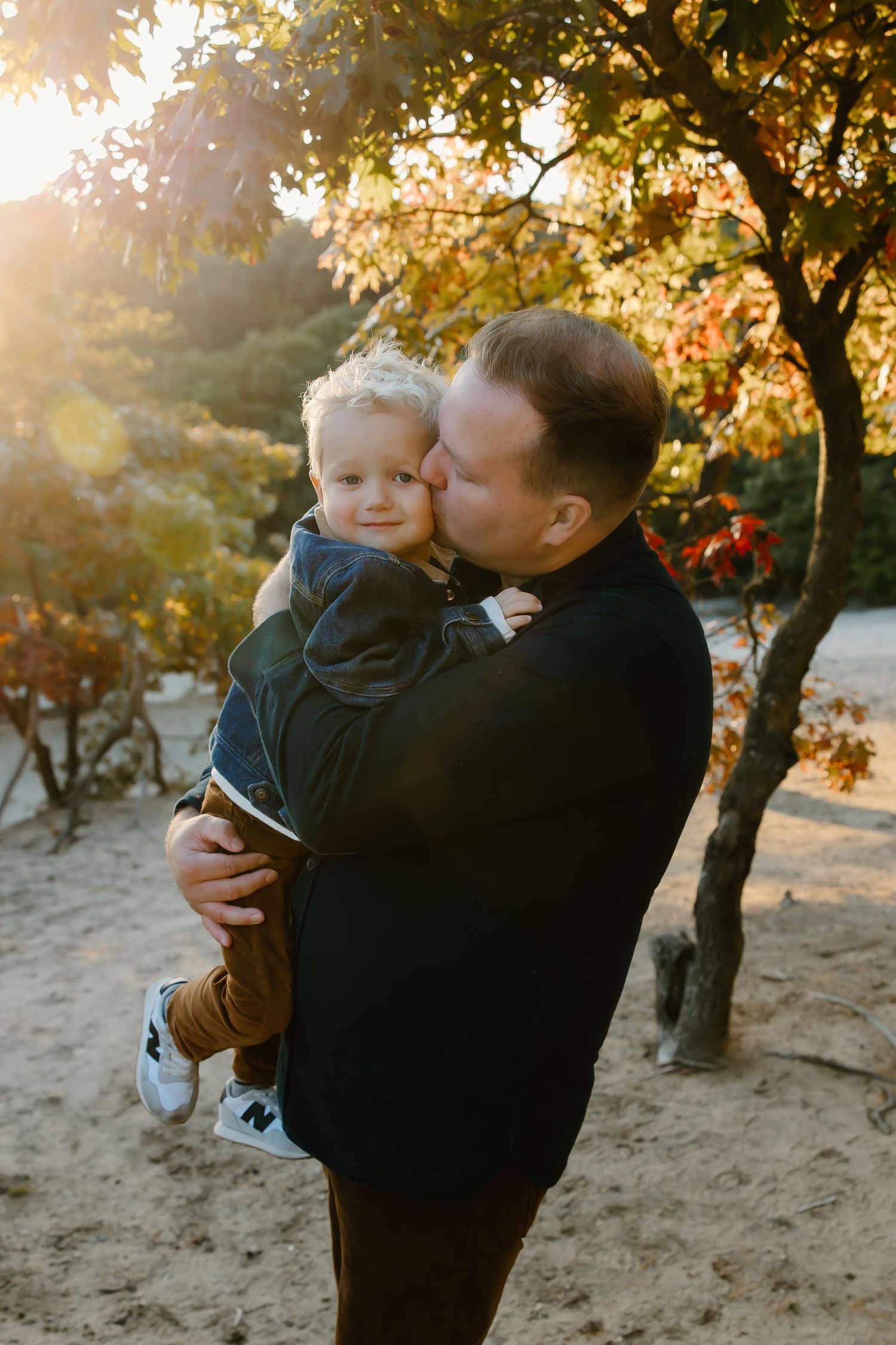 Family shares tender moments during golden hour photoshoot in autumn woodland setting.
