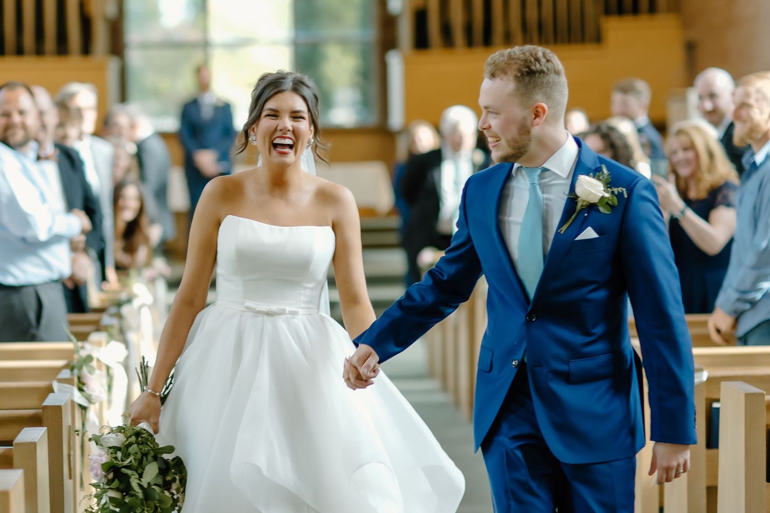 Joyful newlyweds walk down the church aisle as guests look on with smiles.