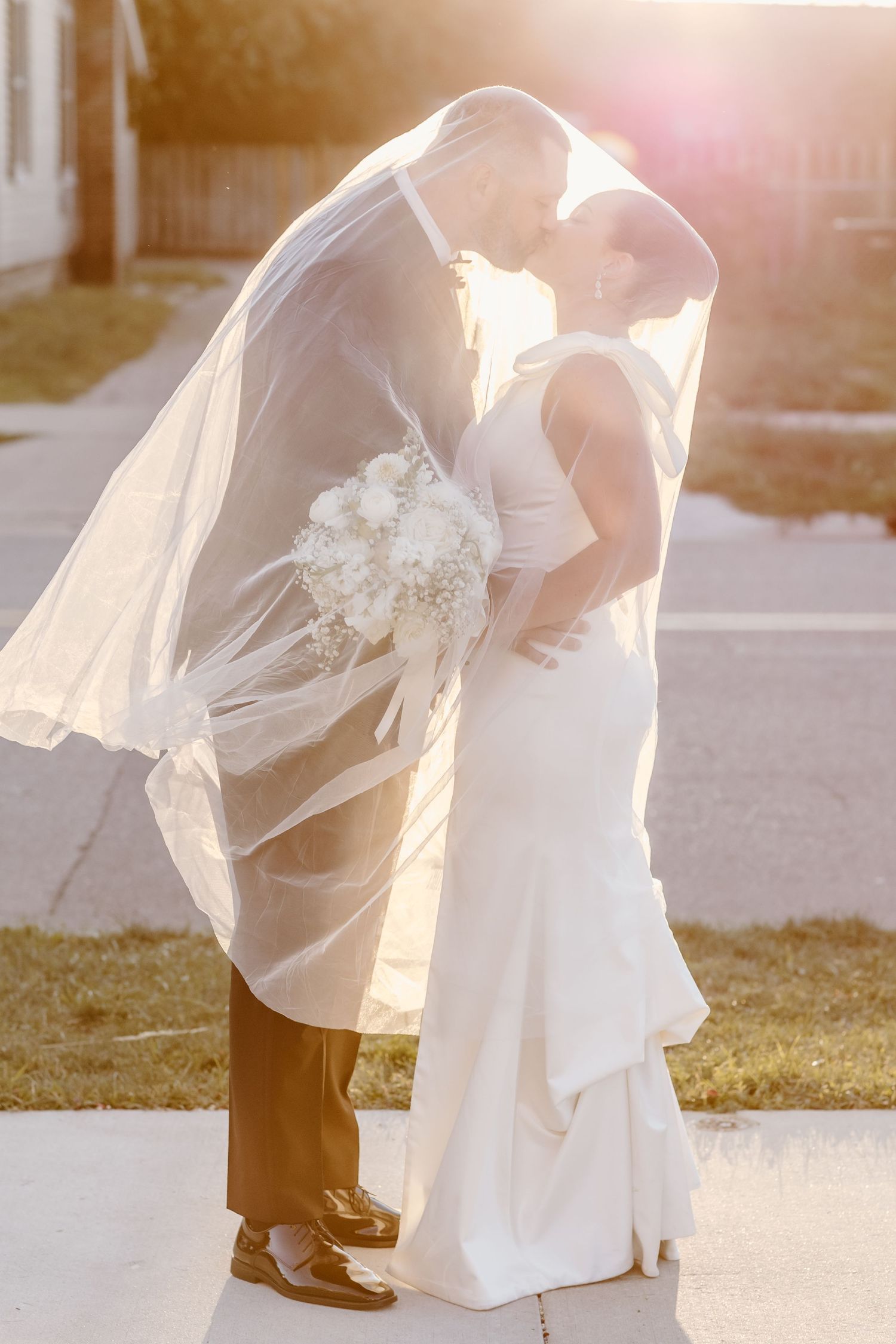 Flowing white wedding dress and veil swirling in elegant motion against sunlit background.