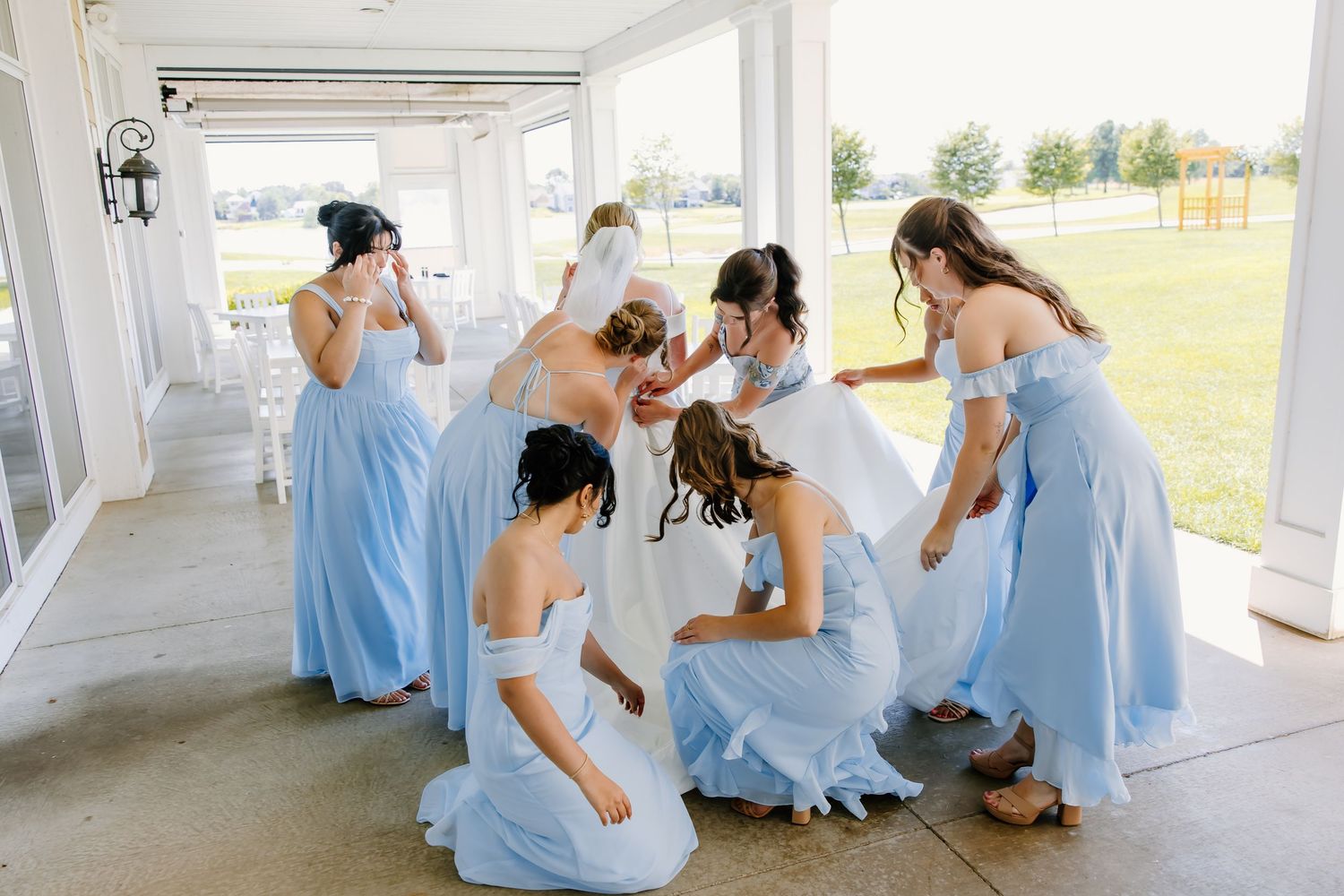 Bridesmaids in light blue dresses sit together on a covered porch during a wedding celebration.