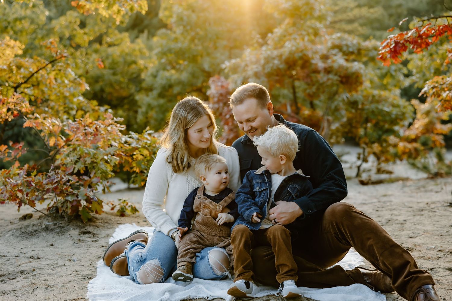 A family relaxes together on a white blanket during an autumn photoshoot.