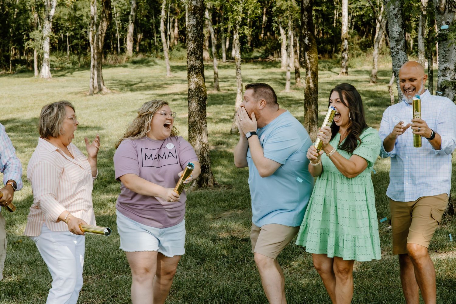 A group of people enjoying a casual outdoor gathering in a wooded area on a sunny day.