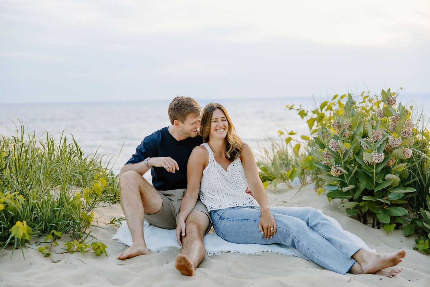 A romantic beach photoshoot featuring a couple relaxing on white sand near coastal vegetation.