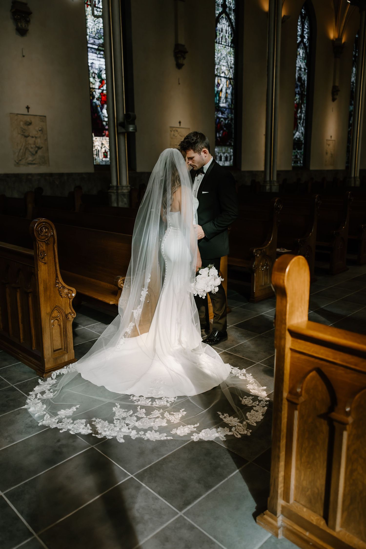 Dramatic low-angle view of a wedding dress train and veil on stone church floor.