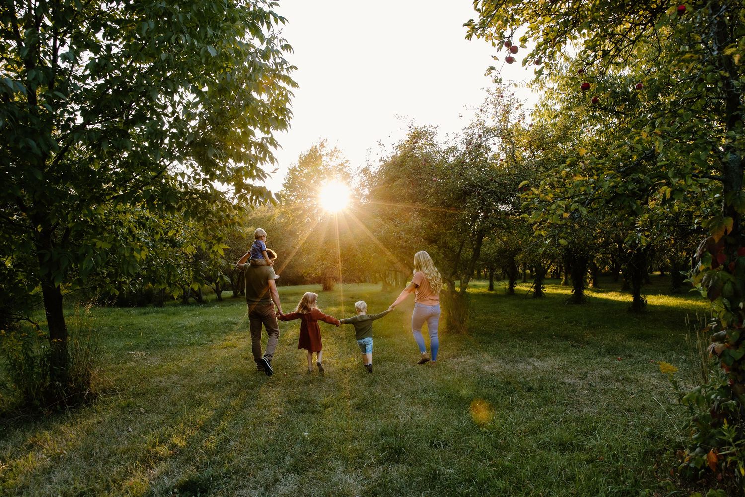 Family silhouettes walking together through a sunlit park during sunset.