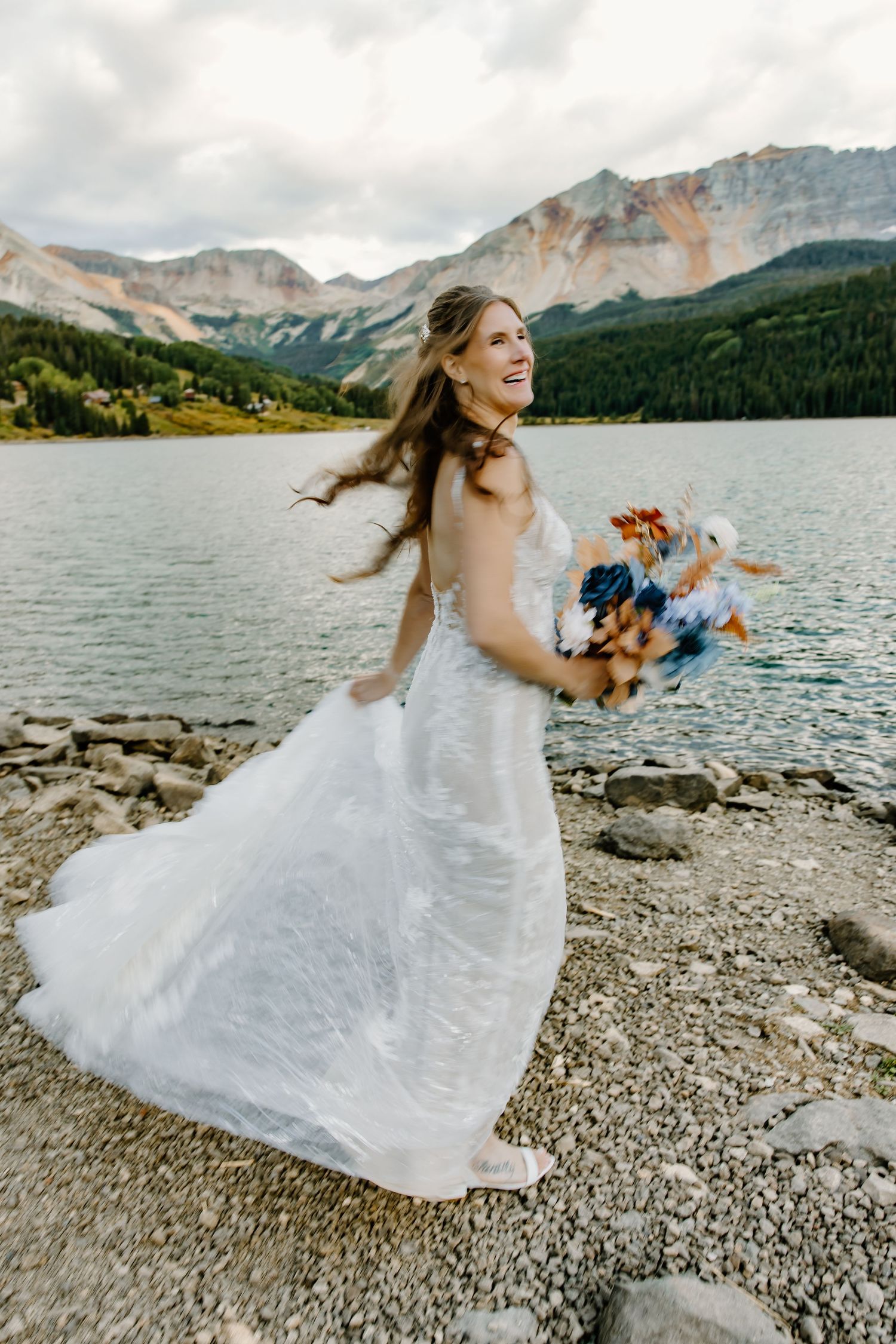 White wedding dress flowing in wind on rocky mountain lakeshore.