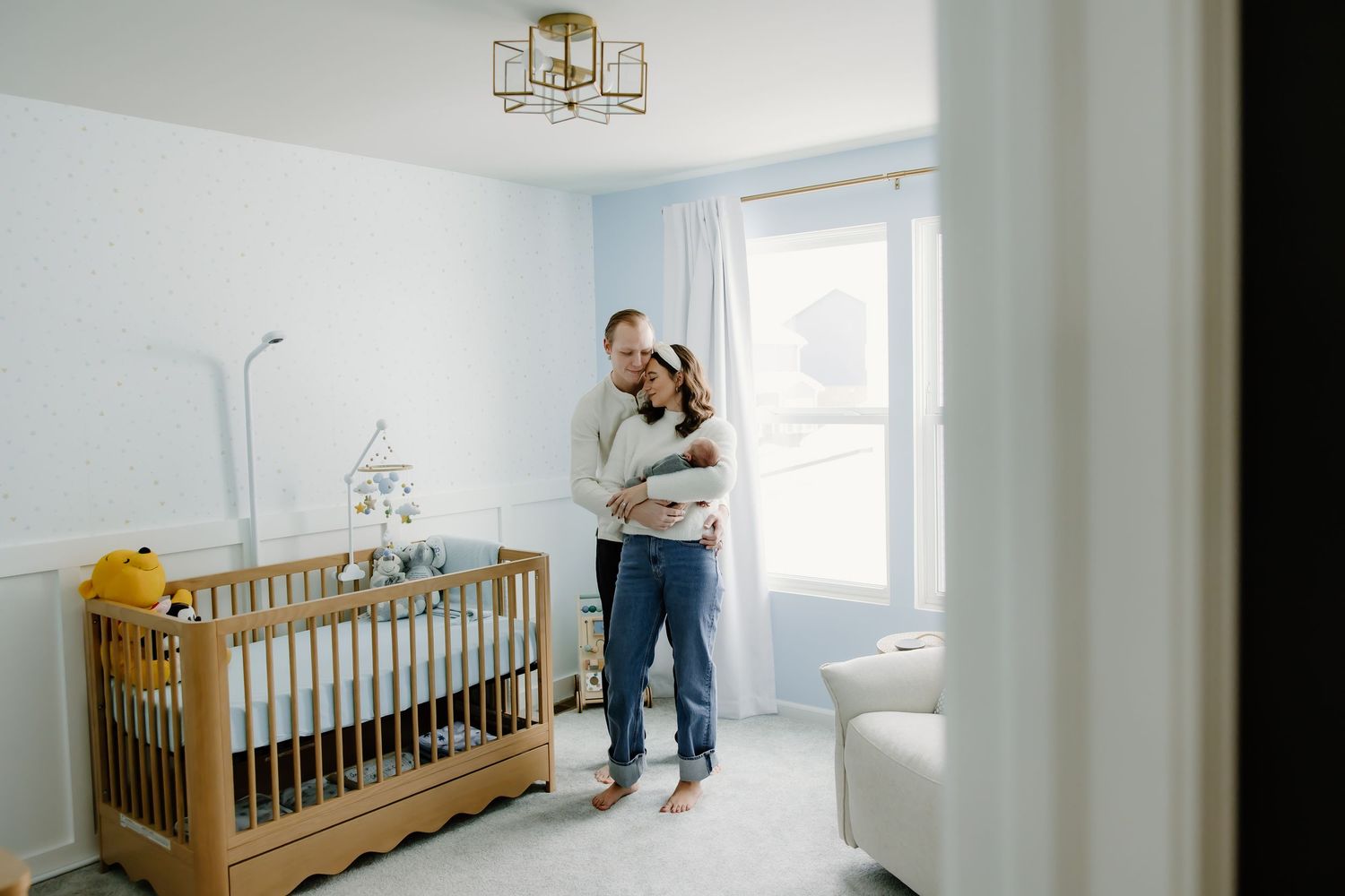 A minimalist nursery room with light blue walls, wooden crib, and modern ceiling light fixture.