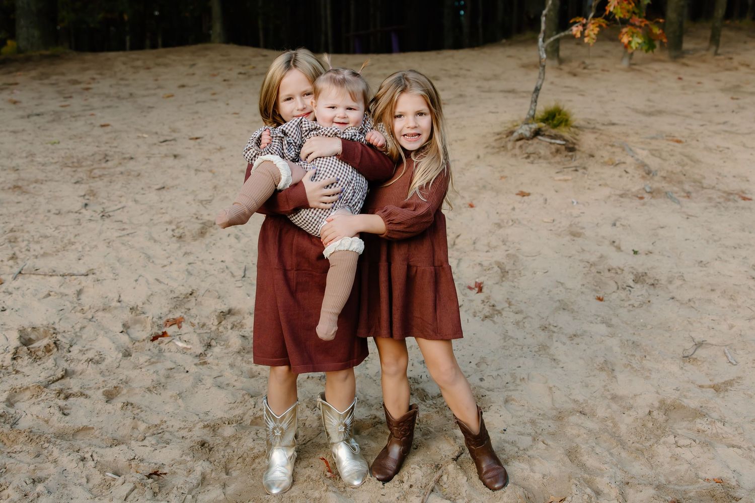 Family wearing burgundy outfits plays together in a sandy wooded area during autumn.