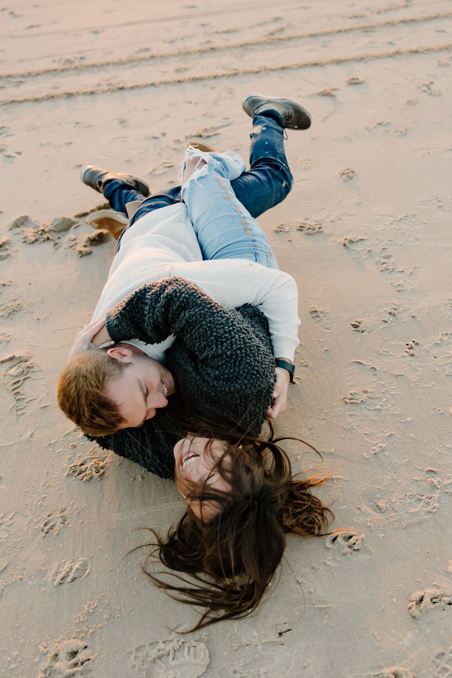 Two people lying on sandy beach during a casual photoshoot.