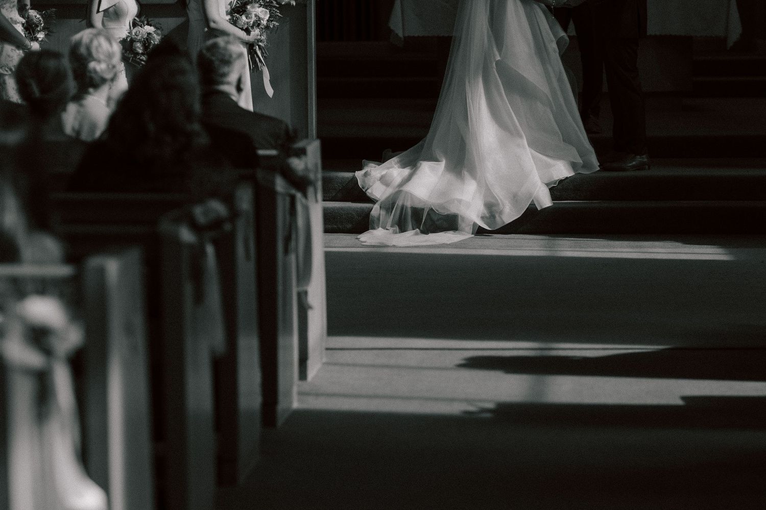 A flowing white wedding dress captured in dramatic black and white lighting inside a church aisle.