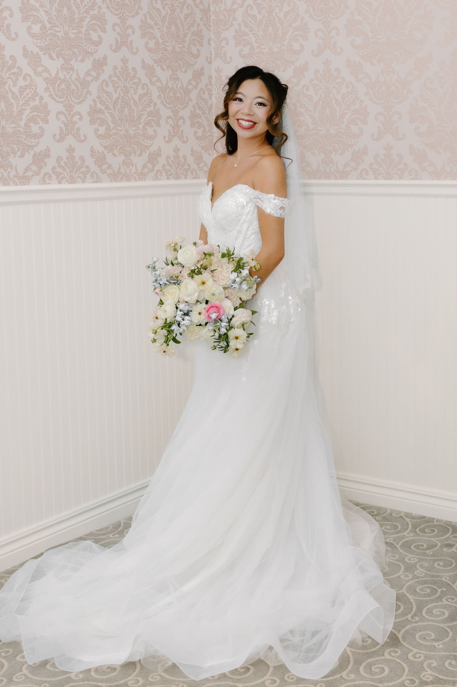 Elegant white wedding gown with flowing train against light wallpaper background.