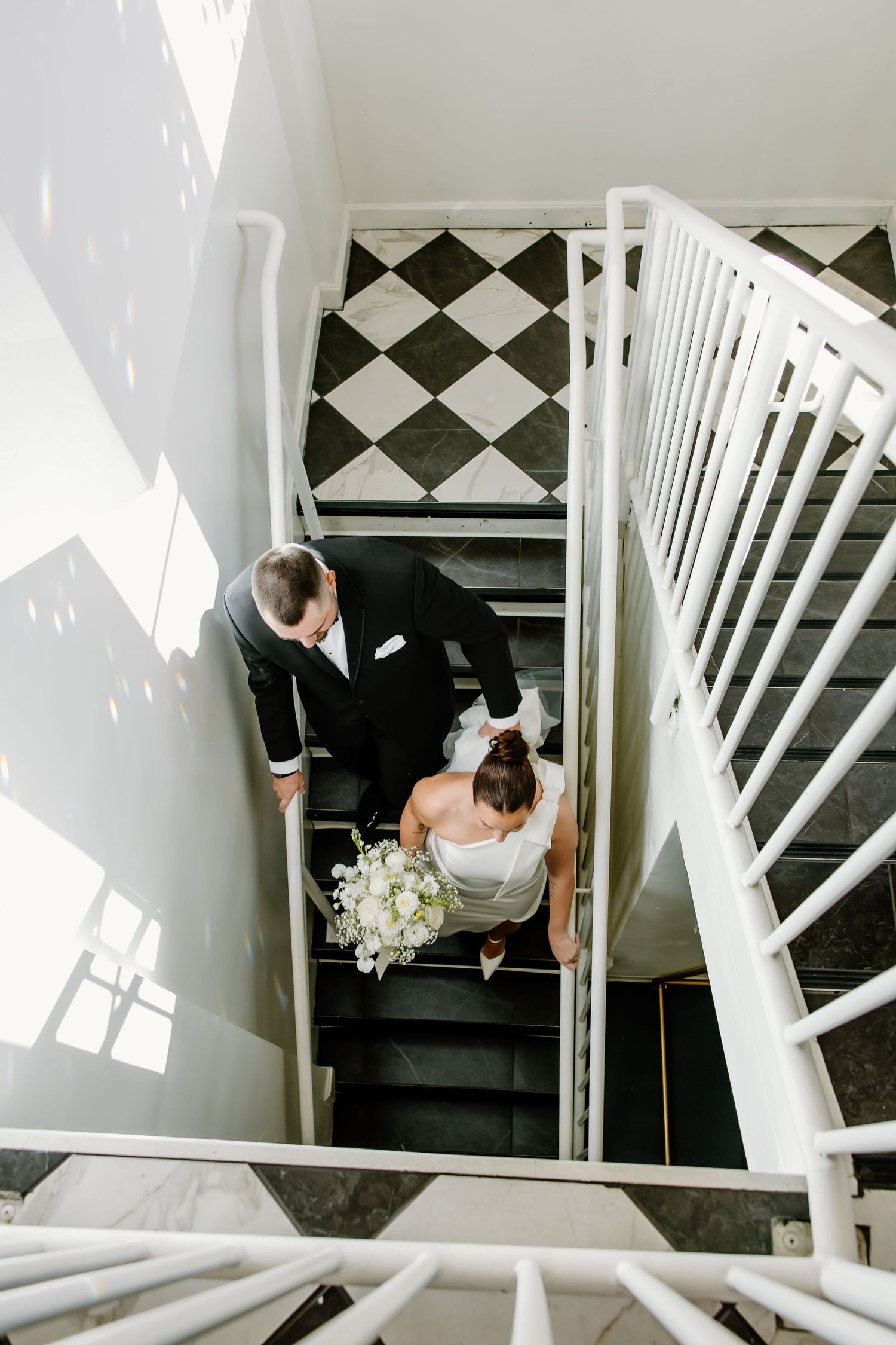 Looking down a white staircase with black and white checkered floor at a wedding venue.
