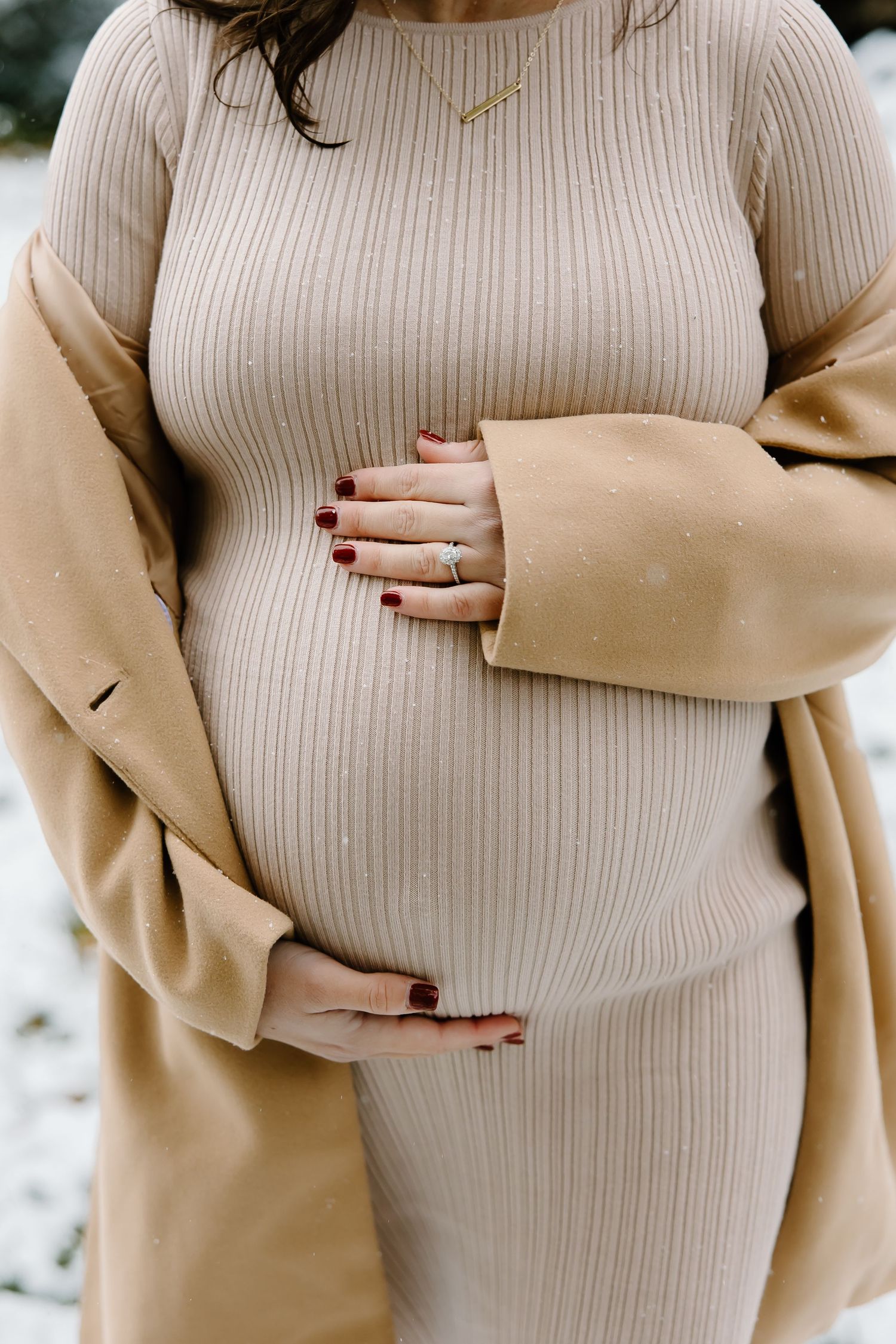 Close-up maternity photos showing hands cradling baby bump in cream ribbed dress.