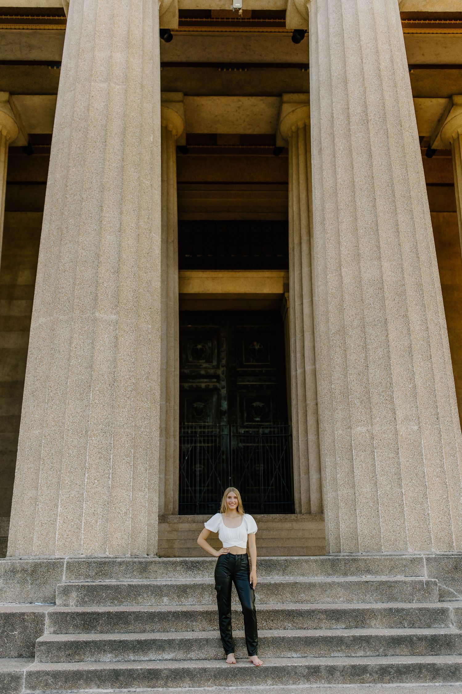A person stands on stone steps between towering classical columns at the entrance of a grand historic building.
