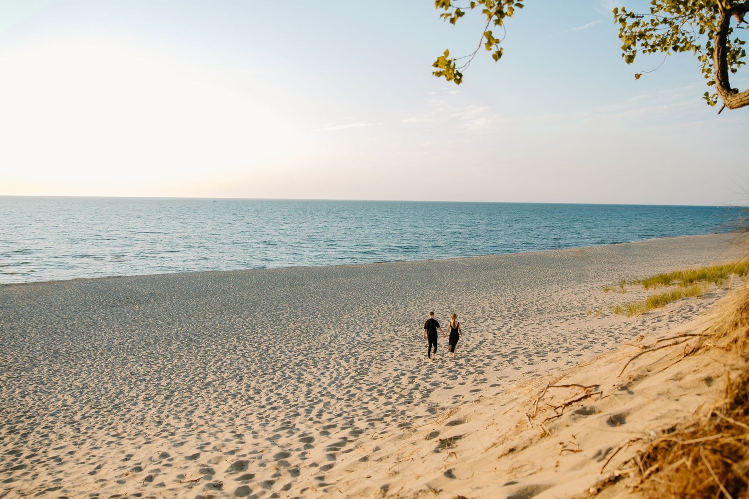 Two silhouettes walking along a vast empty beach with clear blue waters.