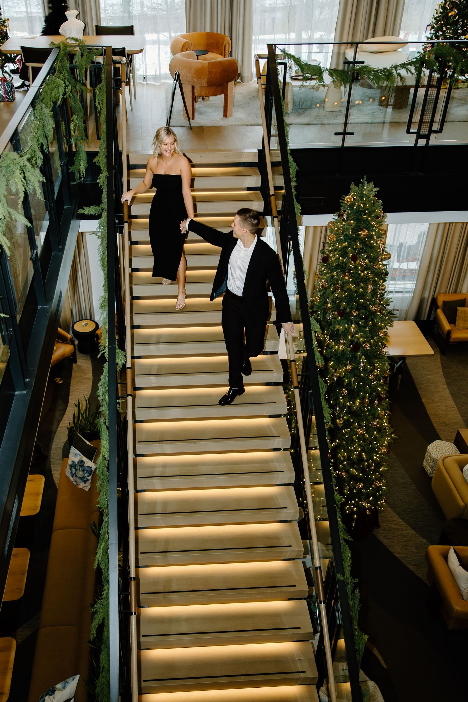 Couple descending illuminated stairs with decorative holiday trees.