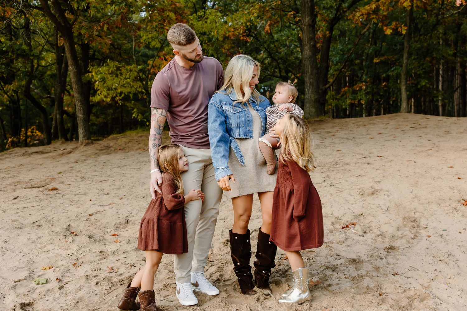 Family enjoys autumn day together on sandy hillside surrounded by colorful fall trees.