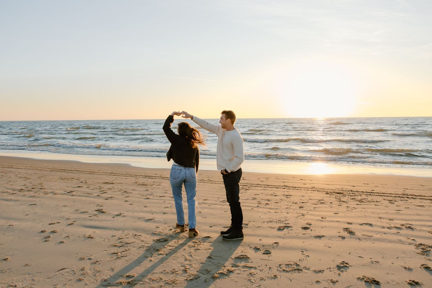 A couple walking along a beach at sunset casting long shadows on the sand.