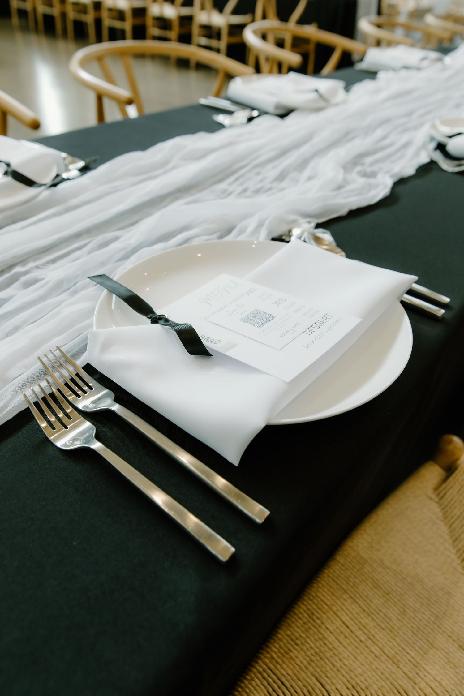 Formal place settings with white plates, silver cutlery, and menu cards on a black tablecloth.