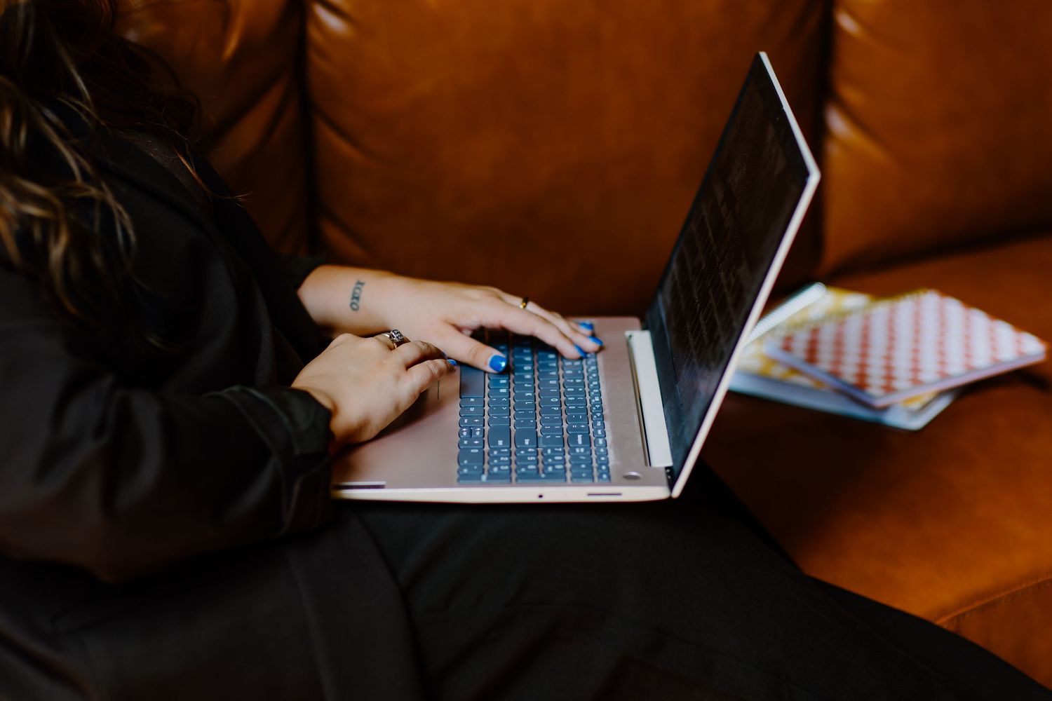 Someone working on laptop while sitting on brown leather couch.