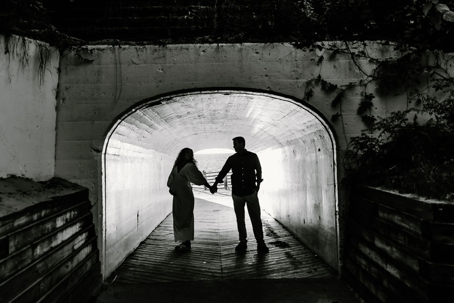 Silhouetted couple holds hands in dramatic black and white tunnel composition.