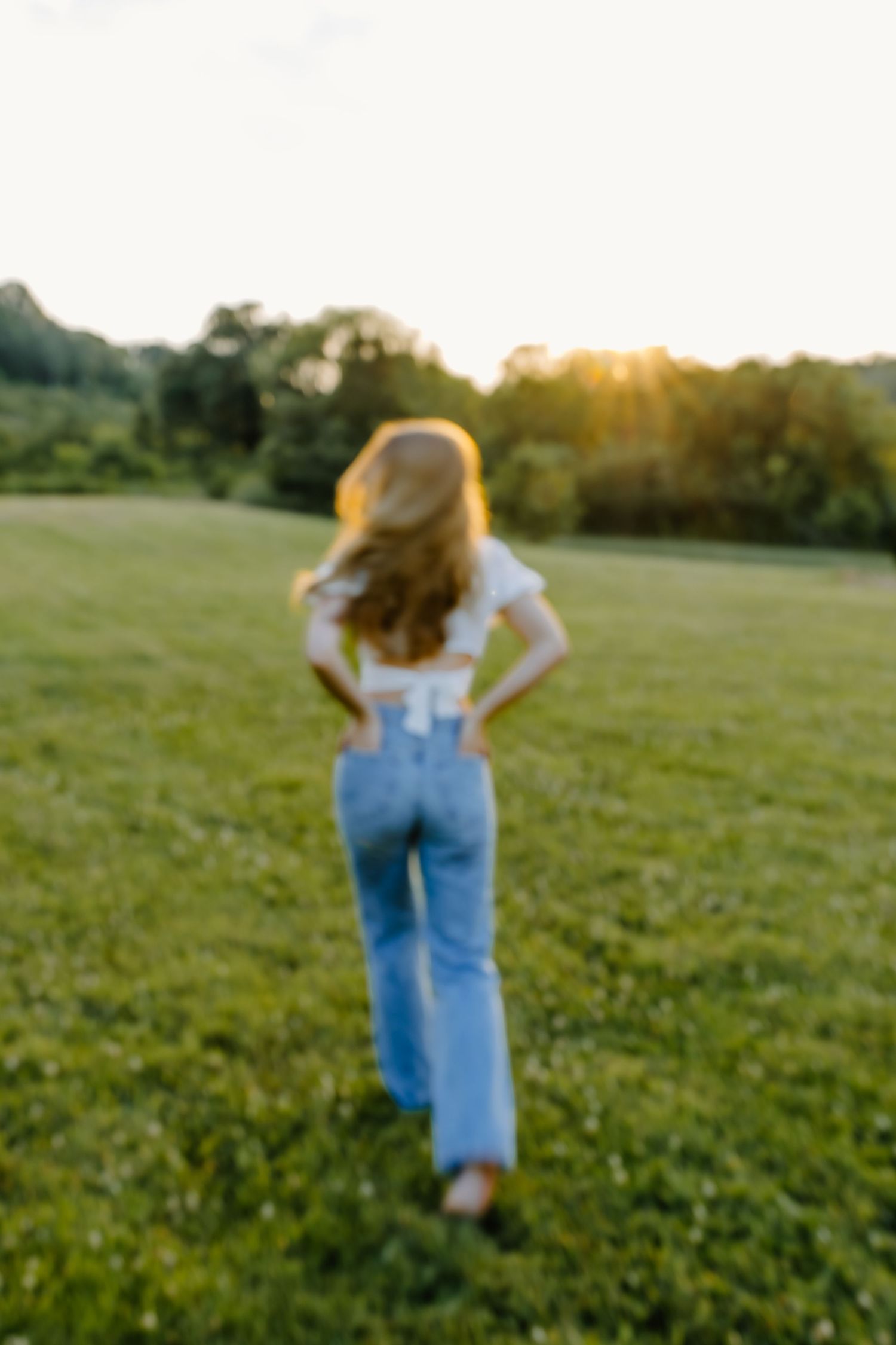 Figure in denim walks through a lush green field at sunset.