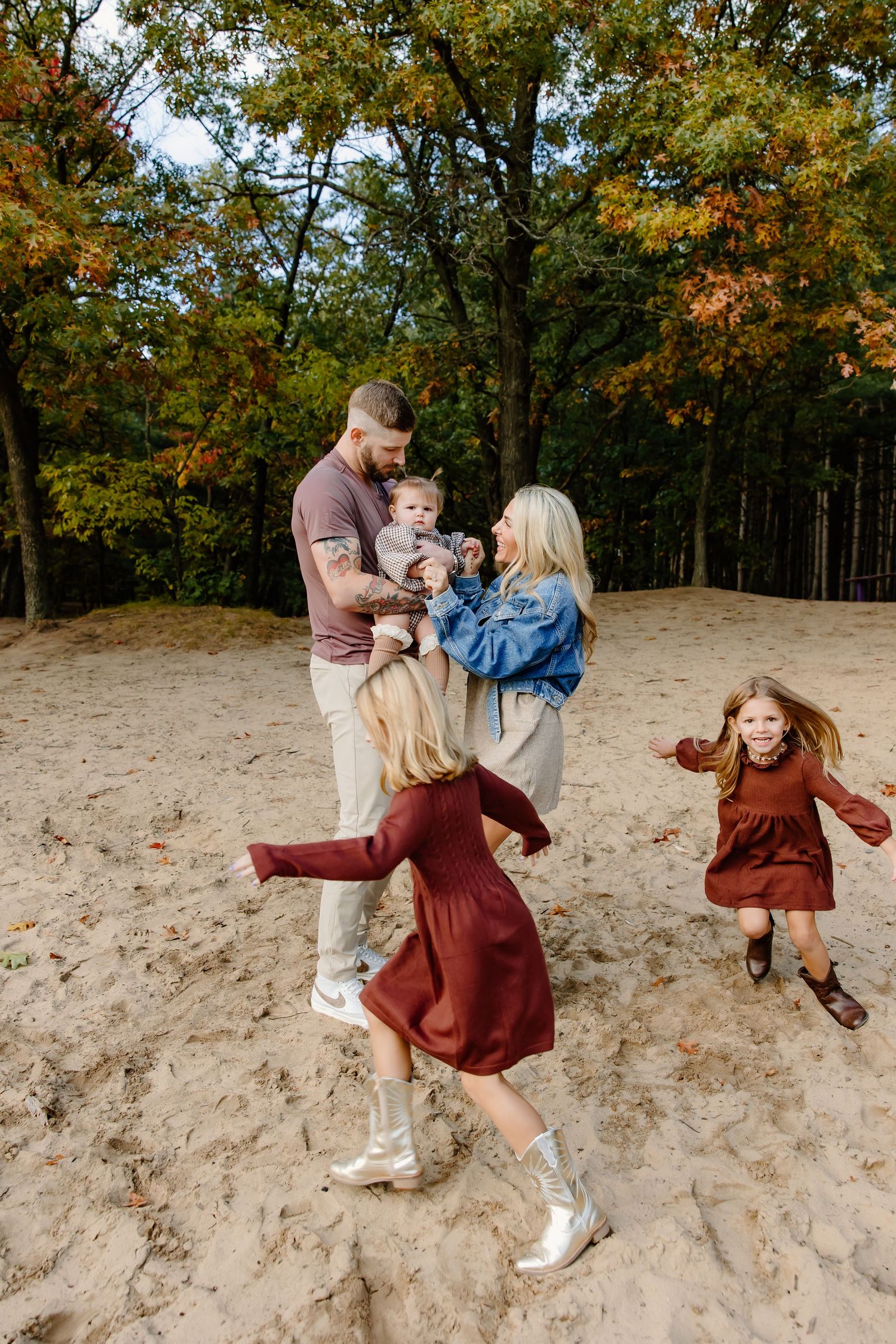 Family playing and spinning together on sandy dunes surrounded by autumn trees.