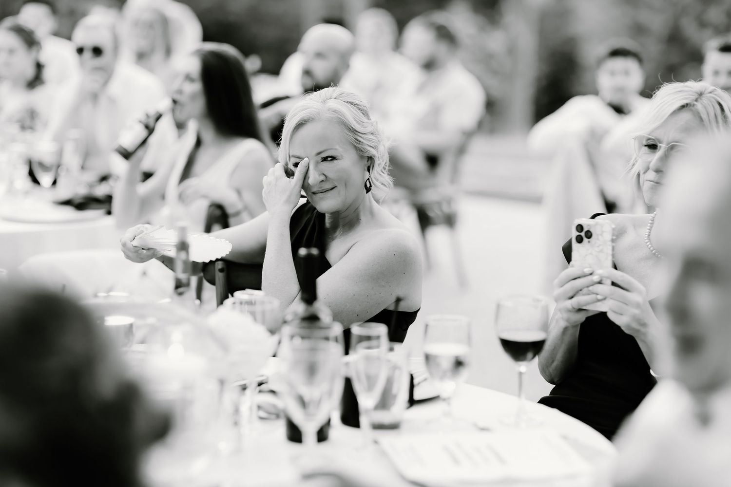 Black and white photo of wedding guests toasting during an outdoor reception.