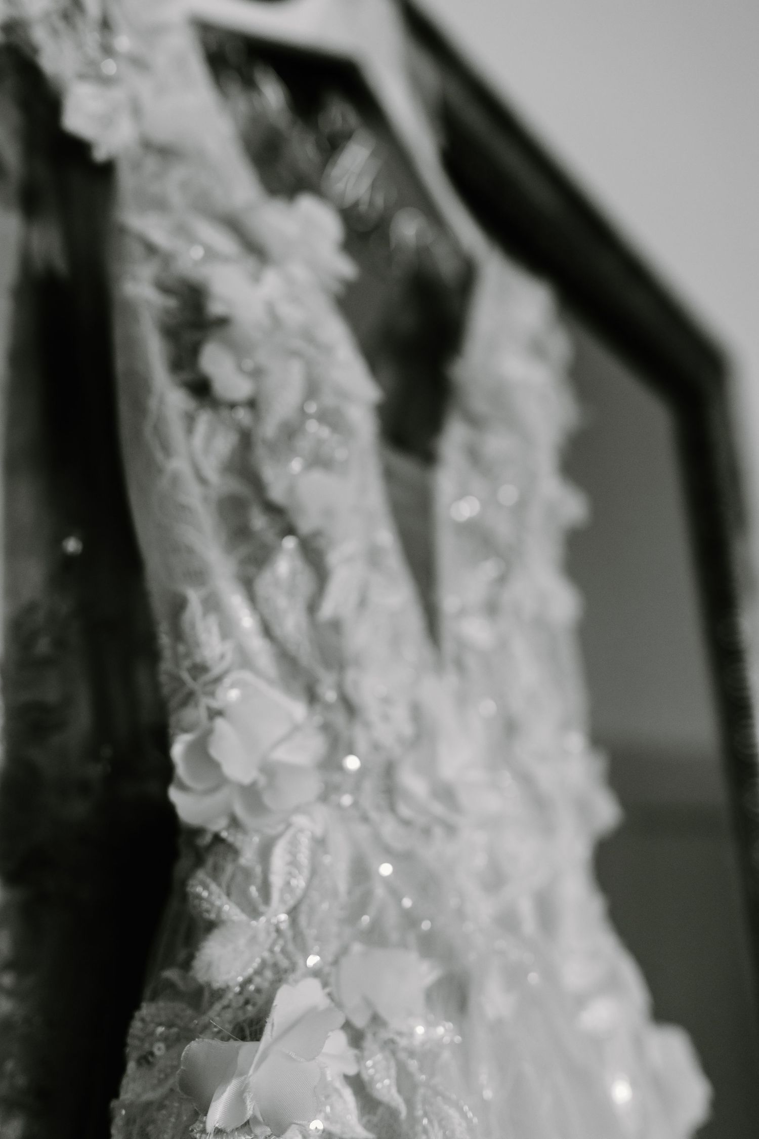 Close-up black and white photograph of delicate white lace details on a wedding dress.