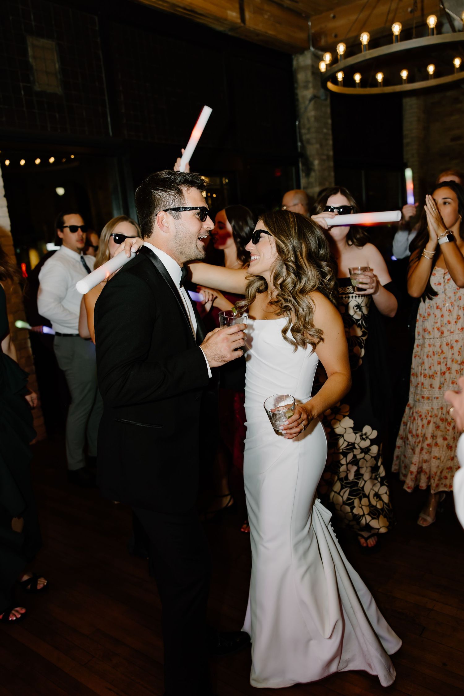 Wedding reception guests dancing and celebrating under string lights at an indoor venue.