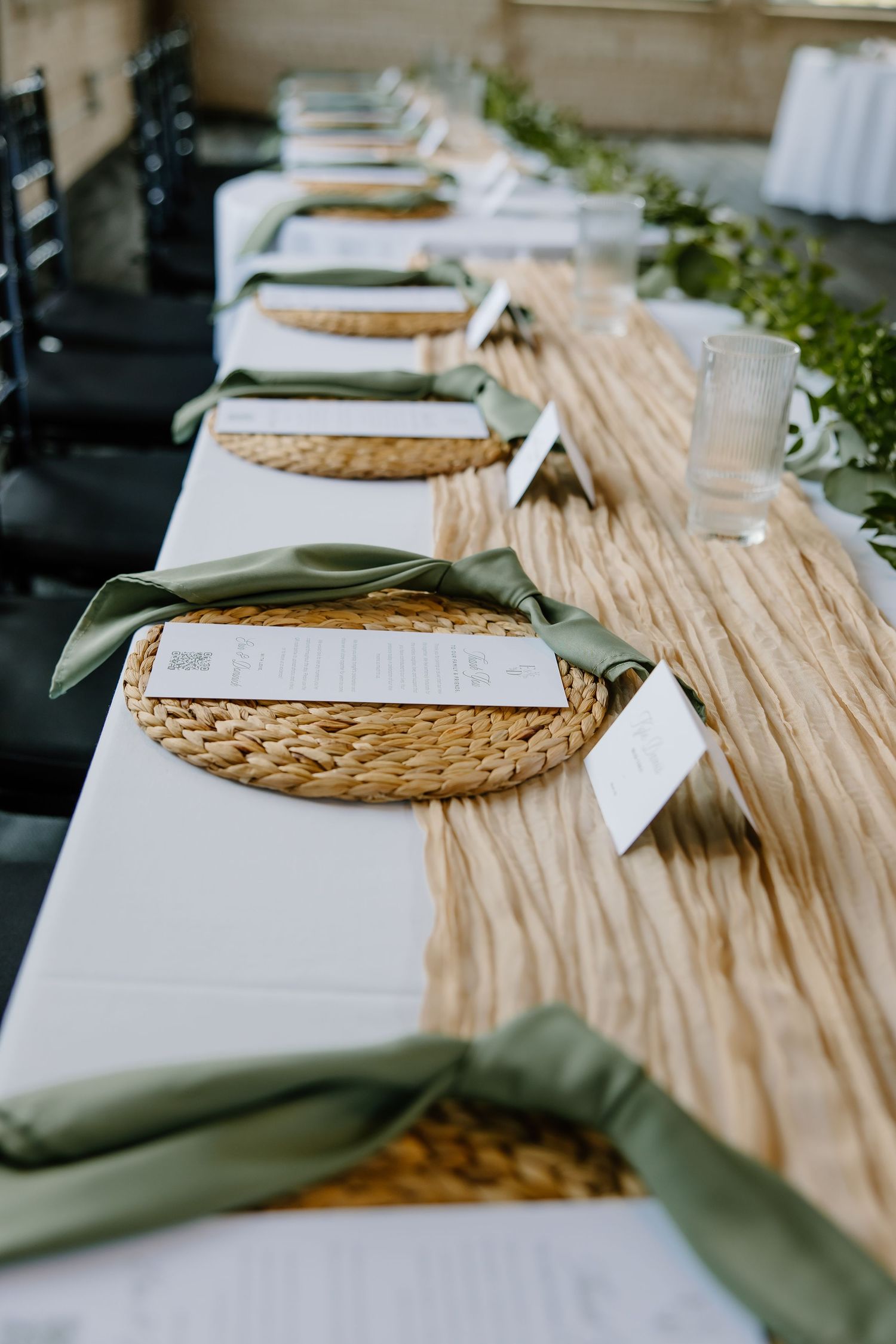 Wedding table settings with woven charger plates and white linens on a textured tablecloth.