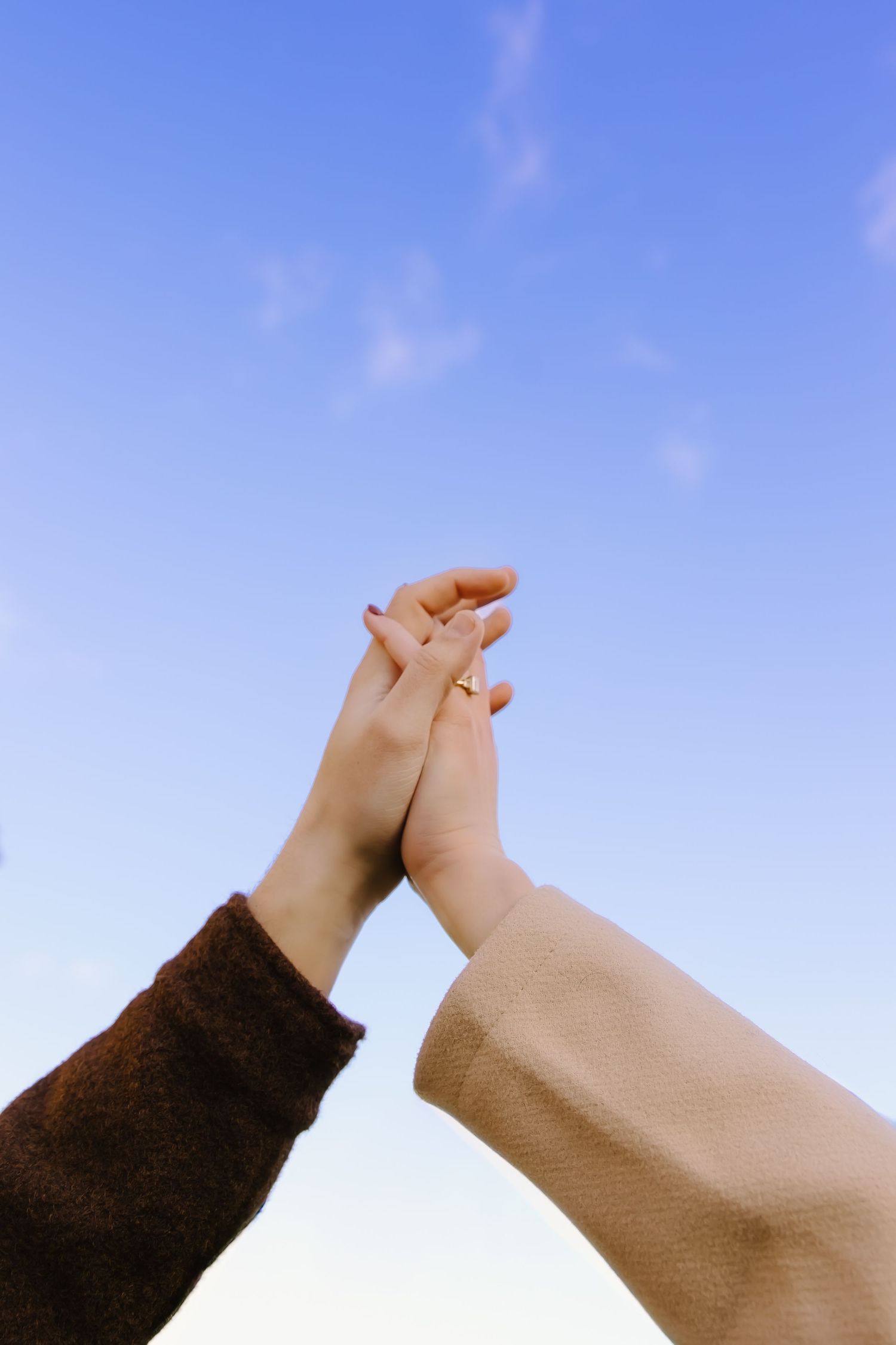 Two hands reach towards a bright blue sky creating a heart shape.