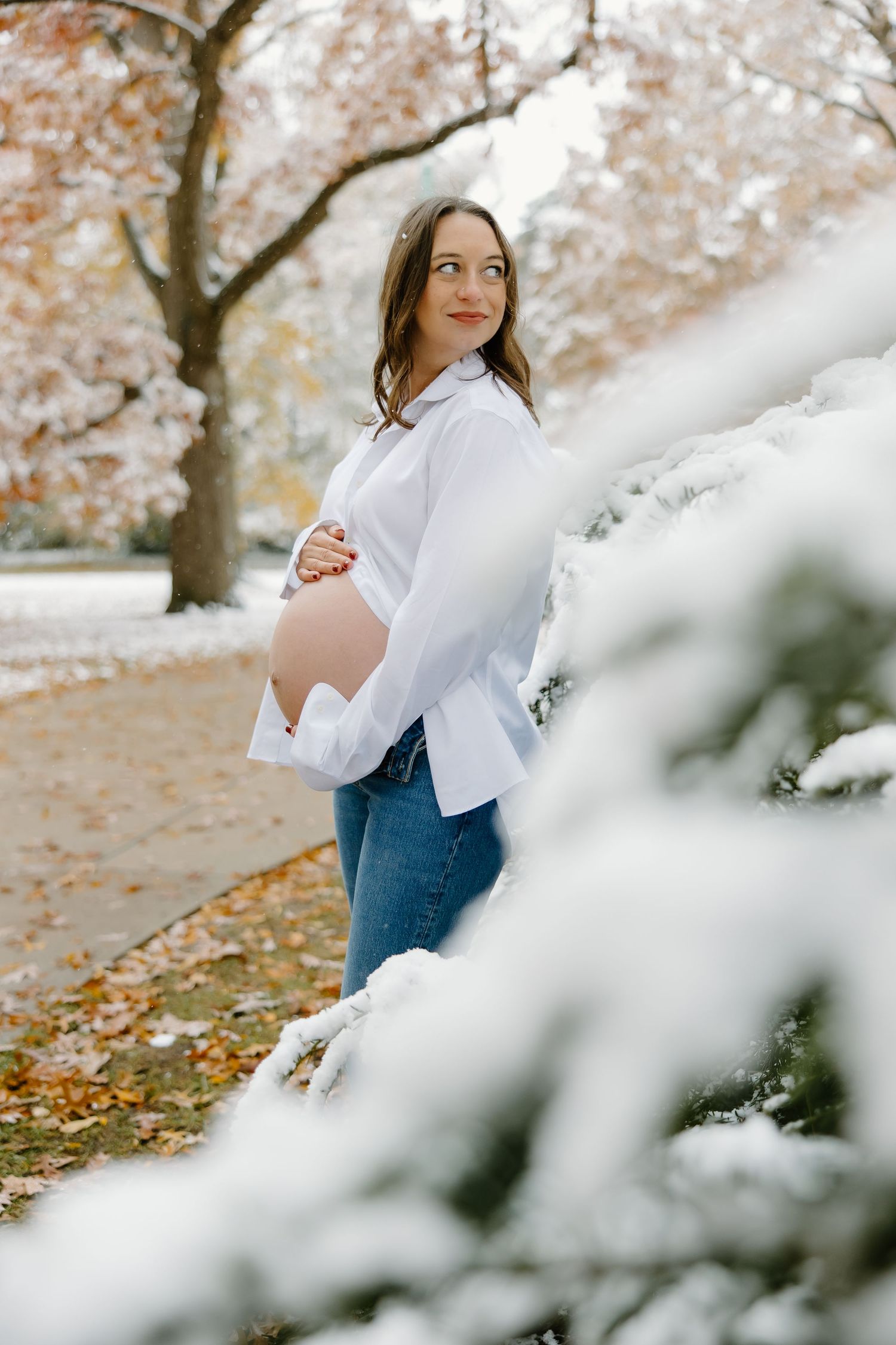 Person in jeans and white top standing among cherry blossoms in a snowy setting.