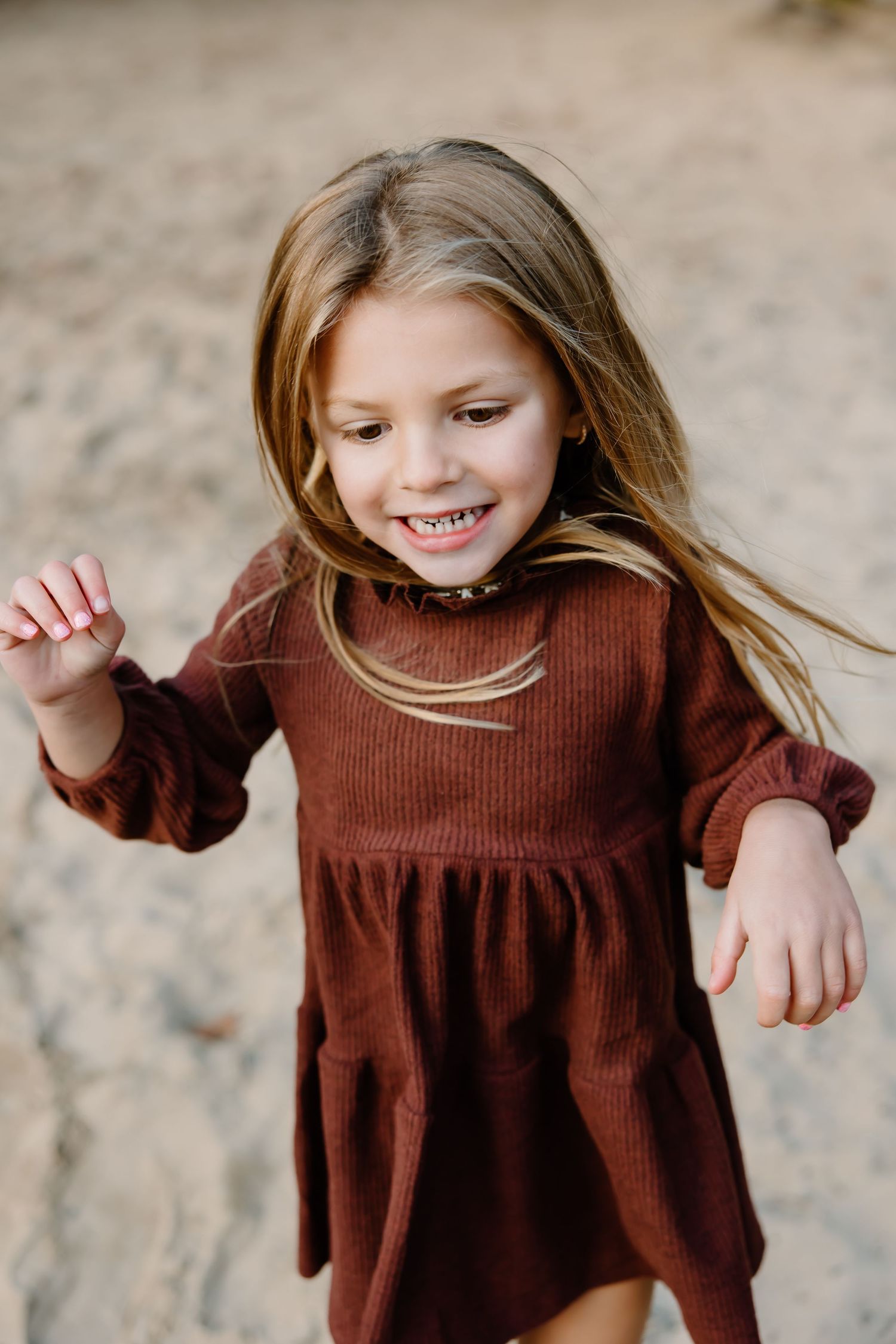 Child in burgundy sweater dress shows joyful expressions against natural autumn backdrop.
