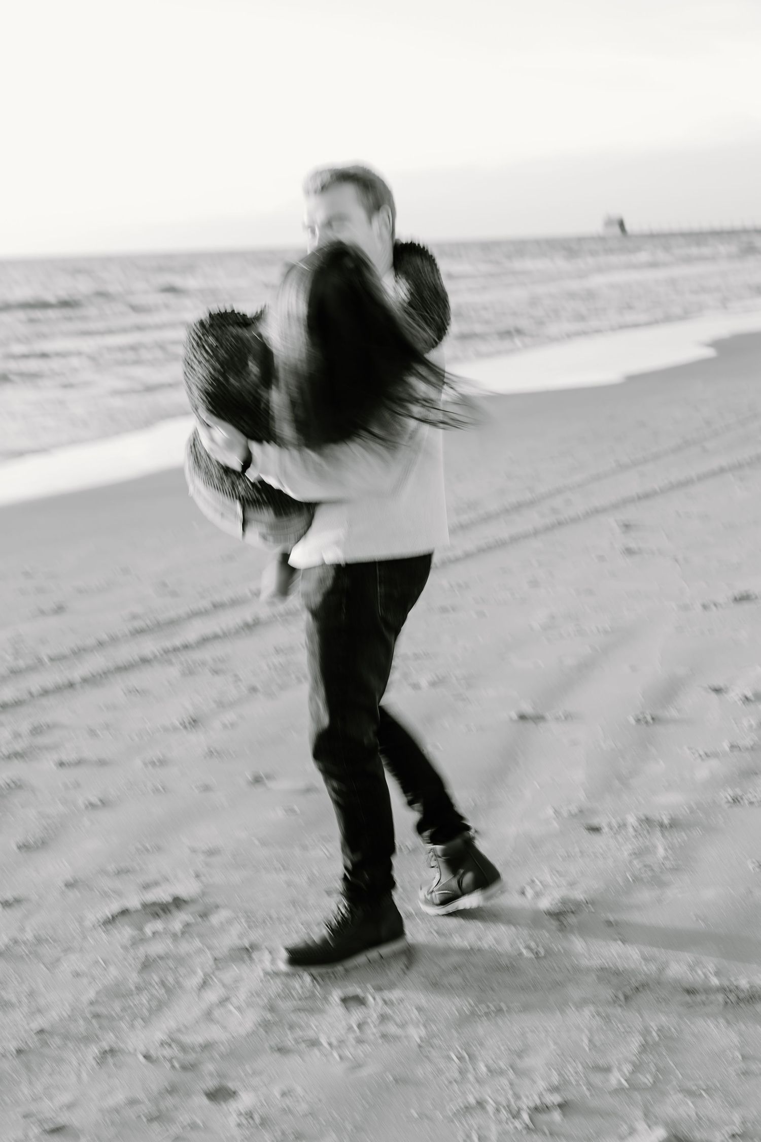 Black and white photo of two people dancing playfully on a beach.