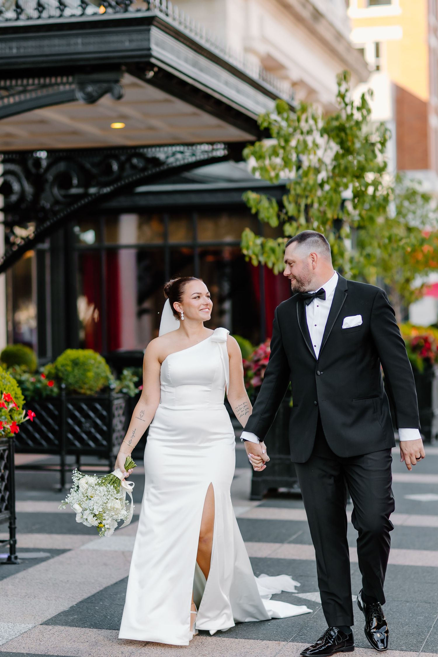 A wedding couple walks together outdoors wearing classic black and white formal attire.