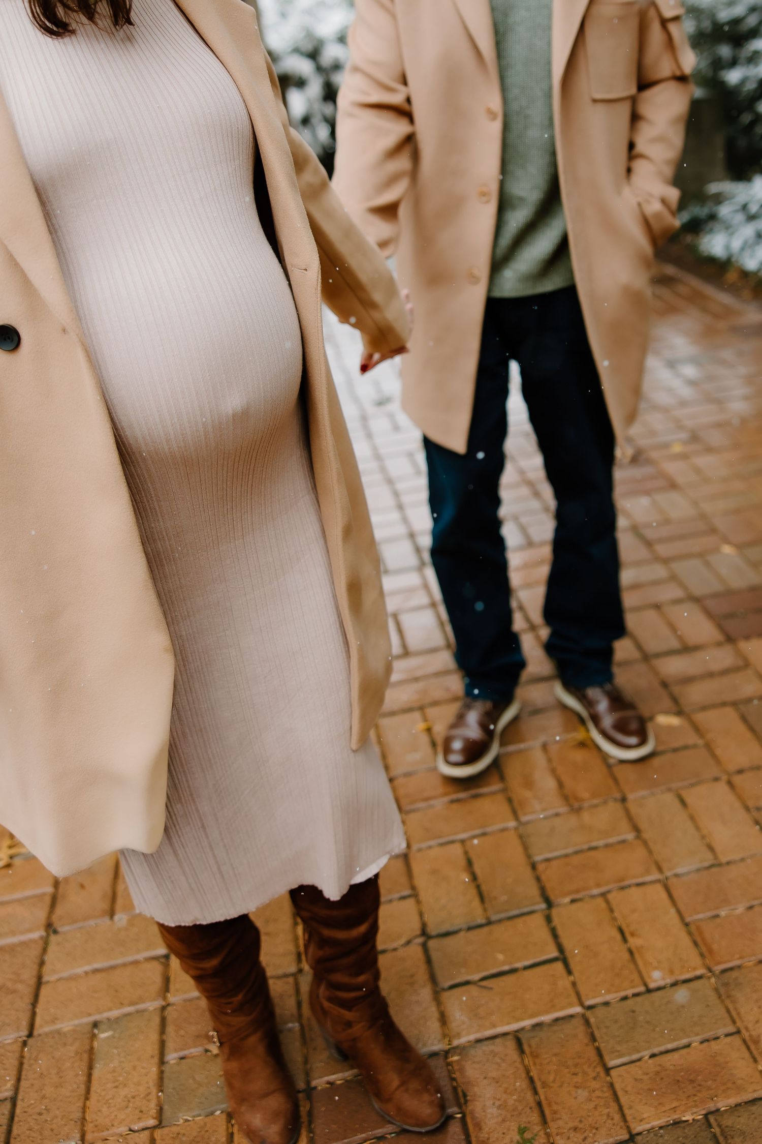 Lower body shot showing brown boots and camel coats on brick pavement.