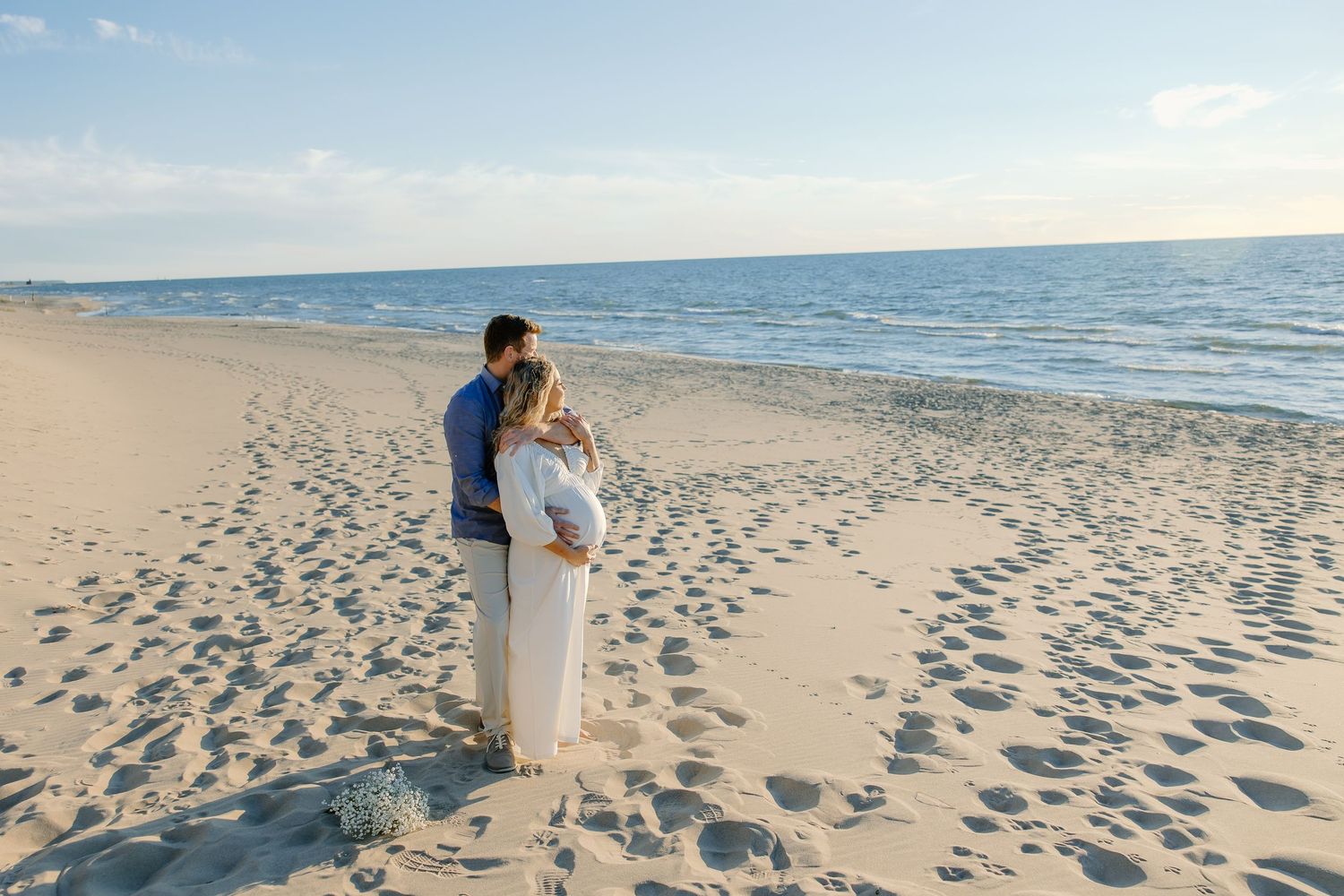 Couple walking together on a sandy beach leaving footprints in their wake during sunset.