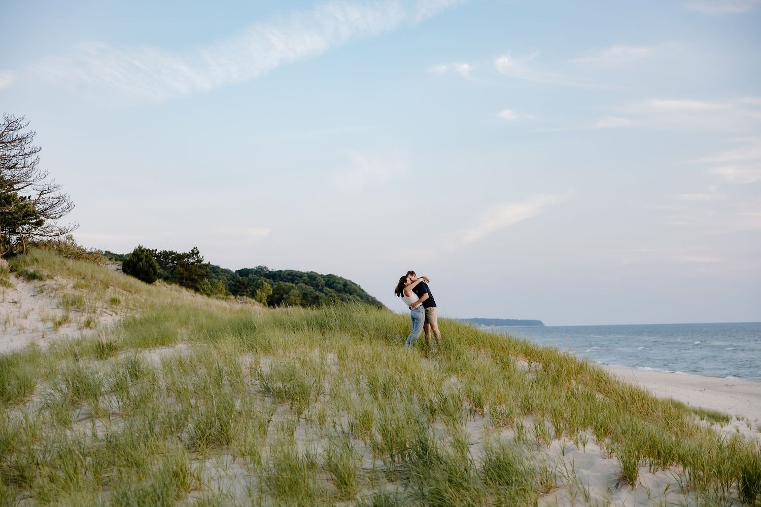 Couple standing on coastal dunes overlooking the ocean on a sunny day.