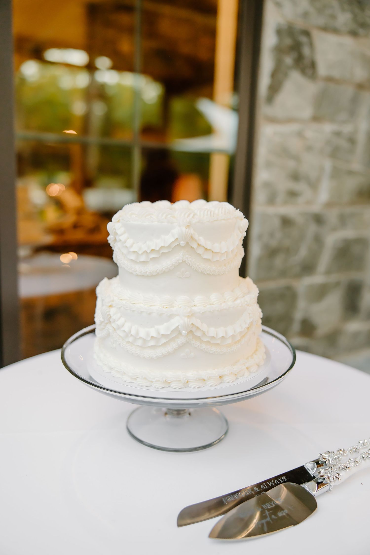 Elegant white wedding cake with delicate piping details displayed on silver cake stand.