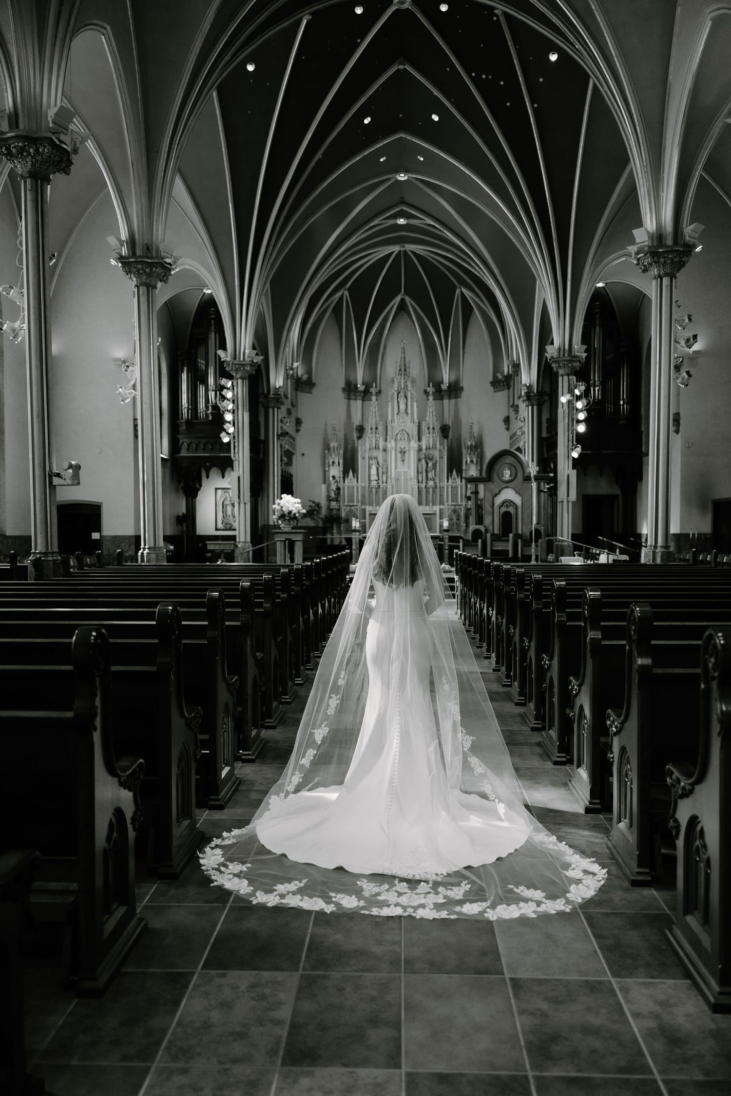 A dramatic black and white photo of a bride in a cathedral with stunning vaulted gothic architecture.