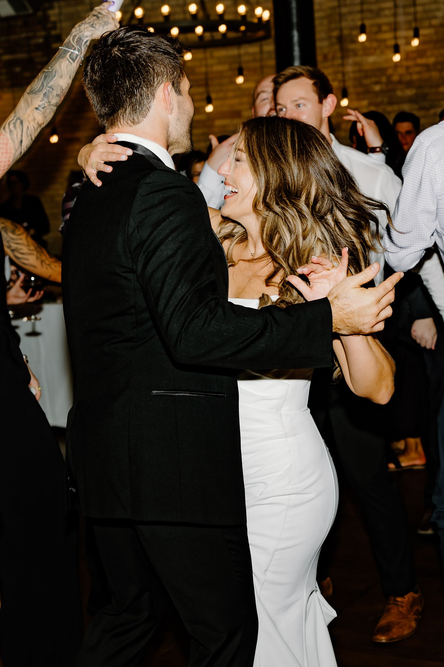 Couples dancing together at a wedding reception with string lights and brick walls visible.
